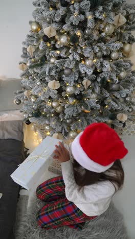 niño abriendo un regalo de navidad bajo un árbol de navidad decorado