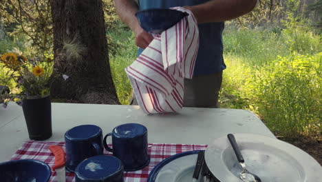 low angle static shot of man drying camping dishes outdoors at campsite