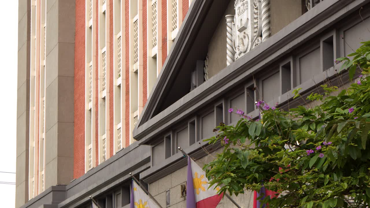 Un plano contrapicado se eleva hacia la arquitectura colonial y banderas nacionales ondeando en Manila.