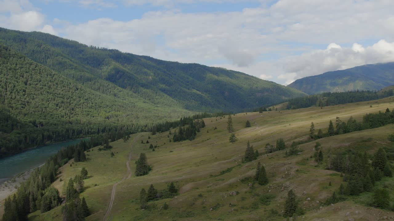 Ampia inquadratura di verdi colline, foresta di conifere e fiume tortuoso nella Valle di Ak-Kem, Repubblica dell'Altai, Russia, sotto un cielo estivo nuvoloso, paesaggio selvaggio e tranquillo