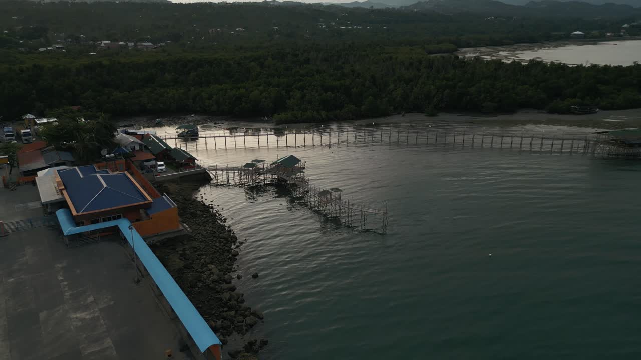 un avión no tripulado desciende al amanecer del puerto de taloot argao en cebu, filipinas, destacando el tranquilo puerto y los barcos atracados por casas empilhadas
