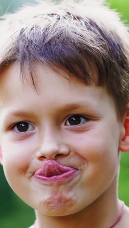 close-up portrait of boy's face outdoors. curious child looking at camera and showing his tongue on blur green background. little boy tries to touch the nose by his tongue. vertical video