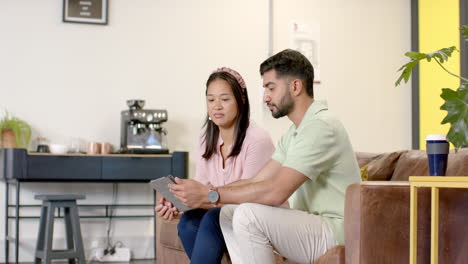 using tablet, colleagues discussing work while sitting on office couch