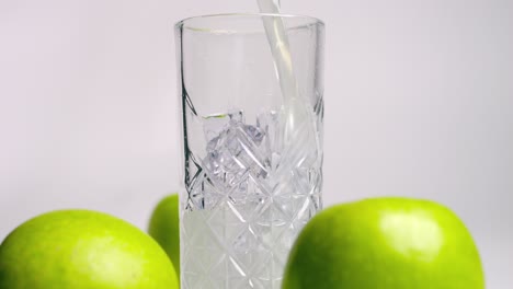 Toma-Estática-En-Cámara-Lenta-Desde-Un-Bonito-Vaso-Lleno-De-Un-Delicioso-Batido-De-Suero-De-Manzana-Verde-Antes-Del-Entrenamiento-O-Entrenamiento-Con-Manzanas-Verdes-Frescas-Circundantes.