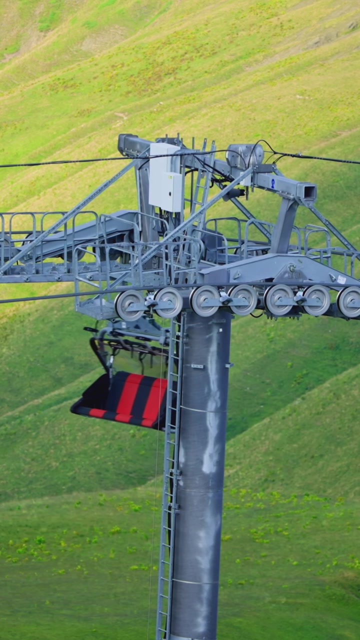 Primo piano di una cabina della seggiovia che passa un pilone su un verde pendio di montagna