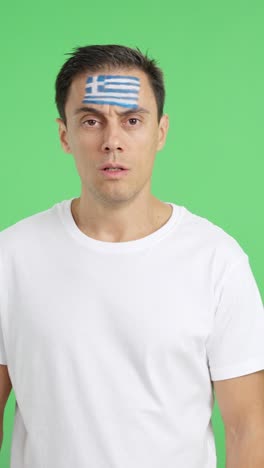 man standing with greek flag painted on face smiling