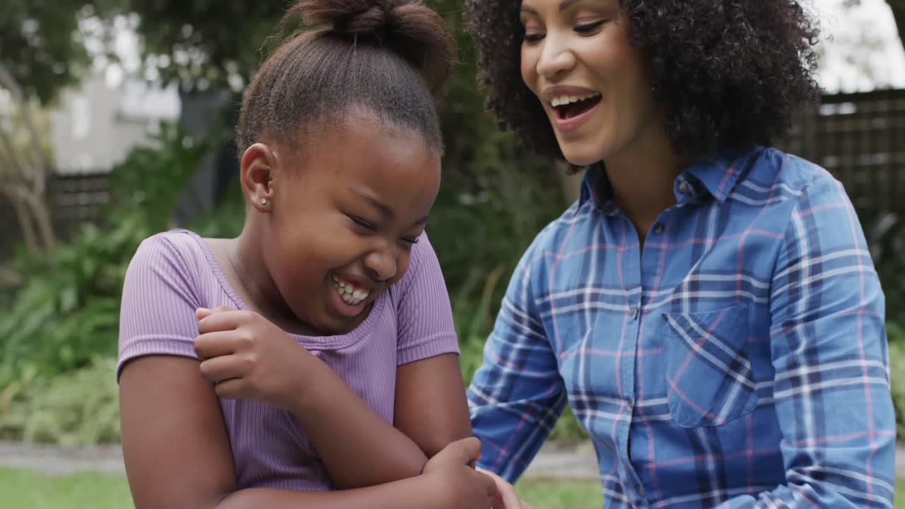retrato de una feliz madre y hija afroamericanas abrazándose y besándose en el jardín, en cámara lenta