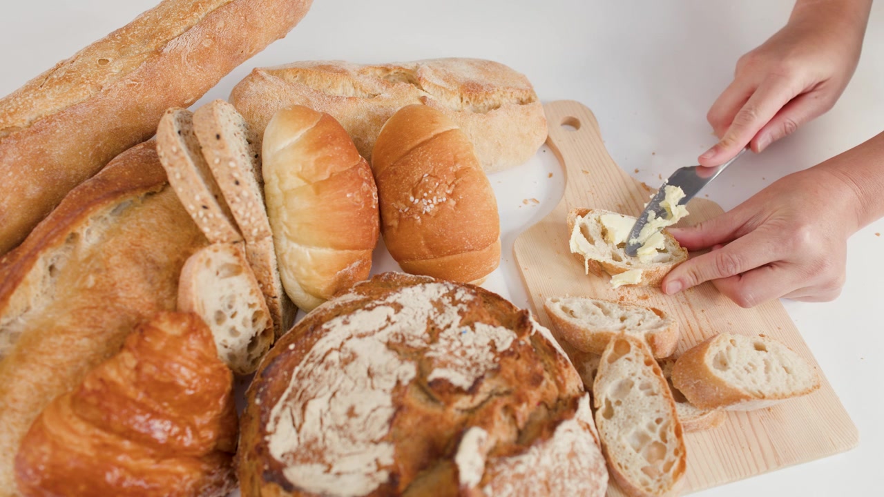 Mani spalmano burro su una fetta di baguette tra pane di pasta madre, croissant e varie pagnotte artigianali.