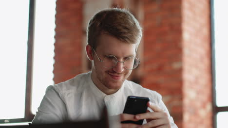 happy man is resting alone in cafe and using smartphone for viewing social media chatting online with friend and smiling