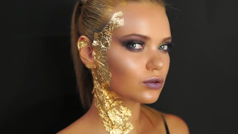 close up of a young woman standing on the black background and looking in the camera. expressive and stylish golden makeup and