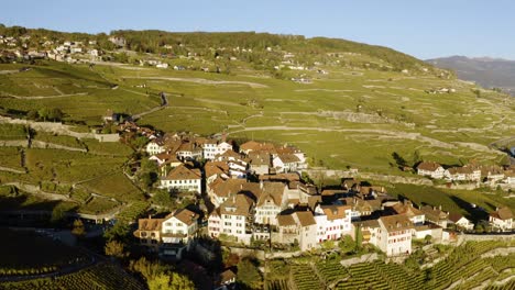 Orbitando-Y-Luego-Sobrevolando-El-Pueblo-Típico-En-El-Viñedo-De-Lavaux,-El-Lago-Léman-Y-Los-Alpes-En-El-Fondo---Colores-Otoñales-De-Suiza-Y-Luz-Del-Atardecer