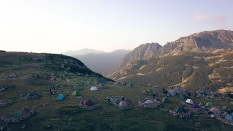 Wide-aerial-drone-footage-of-camera-passing-over-campers-and-tents-flying-towards-cliffs