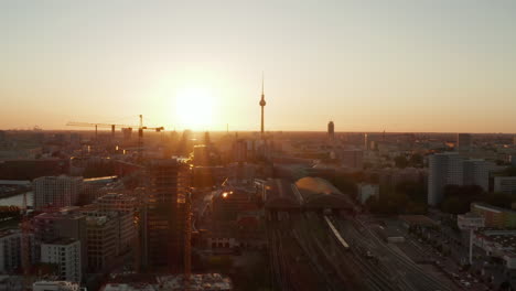 Antena:-Berlín,-Alemania-Sitio-De-Construcción-Con-Grúas-Con-Hermosa-Puesta-De-Sol,-Luz-Solar-Y-Vistas-A-La-Torre-De-Televisión-Alexanderplatz,-Sunflairs