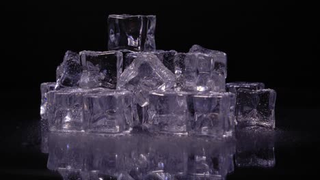 pile of ice cubes with a purple tint rotating against a black background, horizontal static studio shot