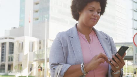 Portrait-of-happy-plus-size-biracial-woman-using-smartphone-in-city