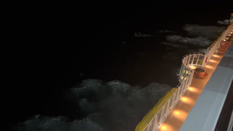 passenger's view overlooking a wooden ship deck and ocean waves during a cruise at night.