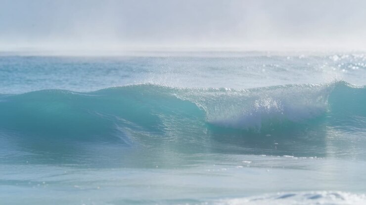 Breaking turquoise ocean wave forming curling lip and whitewater nearshore, with spray and horizon