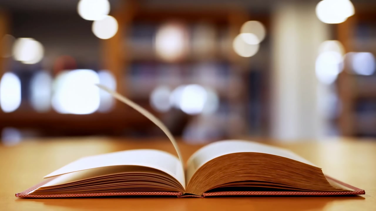 Diverse pagine si alzano, si piegano e si sfogliano da un lato all'altro di un libro aperto, mentre il libro rimane centrato sul tavolo, con luci bokeh calde e librerie sfocate sullo sfondo.