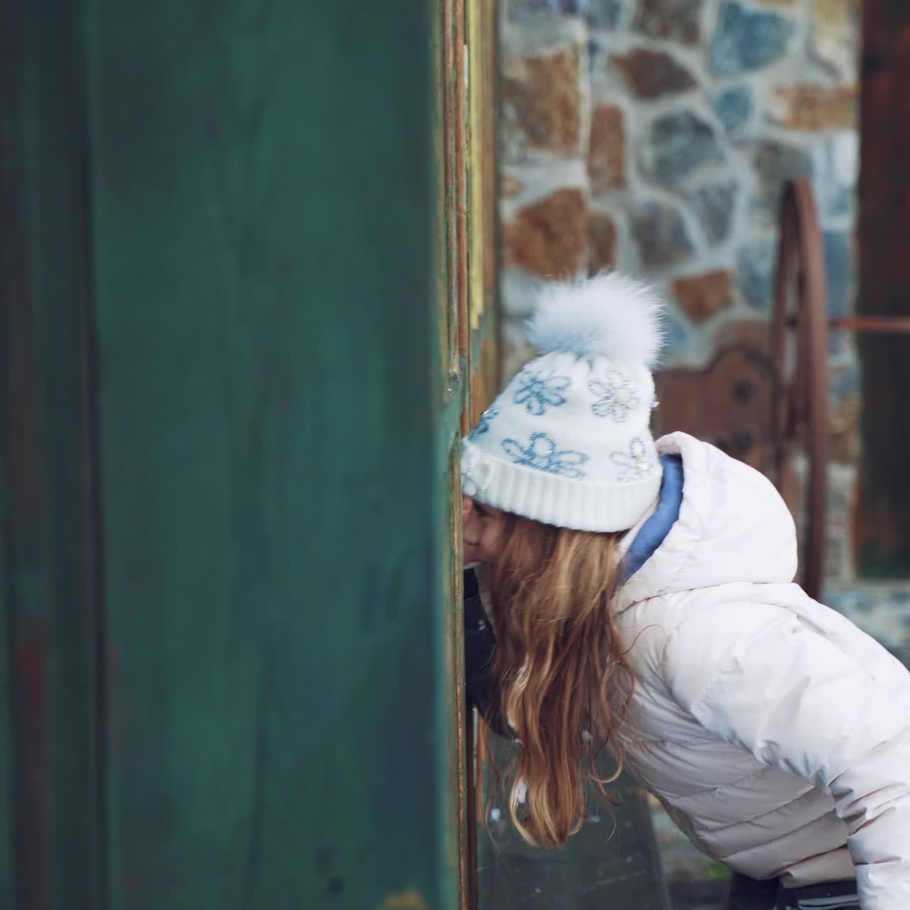 A little girl with an envelope in her hand is peeping through the window to elves at day before the New Year in the street on the background of snow.