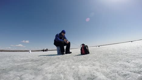 a man seated while ice fishing - wide shot