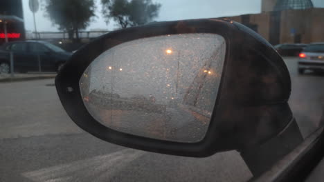 view of a car passing by through blurry wet left side mirror of a parked car on a rainy day - pov, static shot