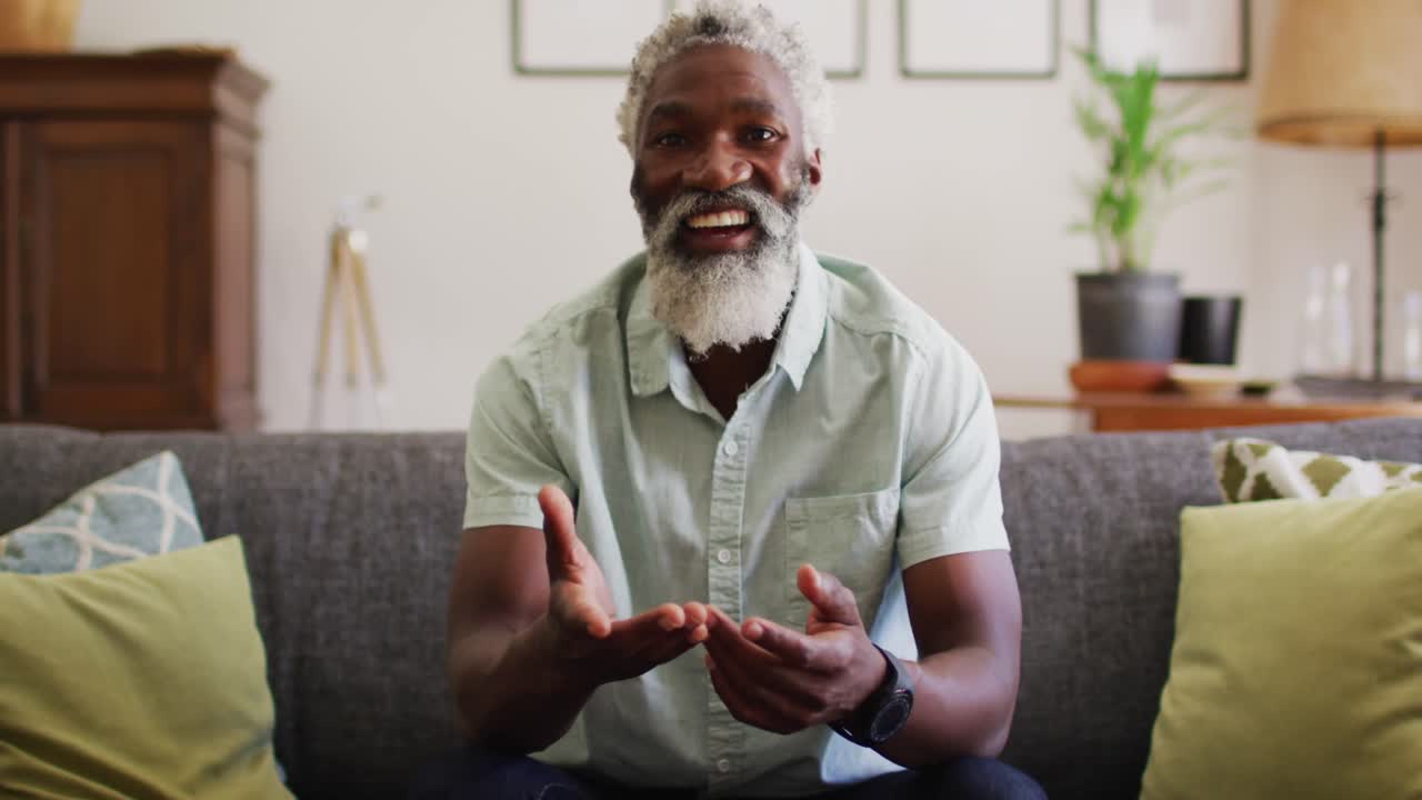 Happy african american senior man sitting on couch making video call smiling and waving