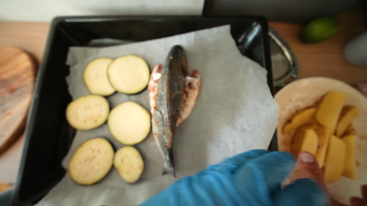 Preparando pescado fresco con berenjena en rodajas y patatas en una bandeja de horno