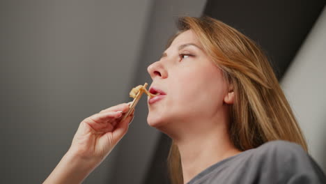 Close up view of young lady enjoying pasta using chopsticks, tilting her head back while eating, relaxed indoor atmosphere with soft blurred background