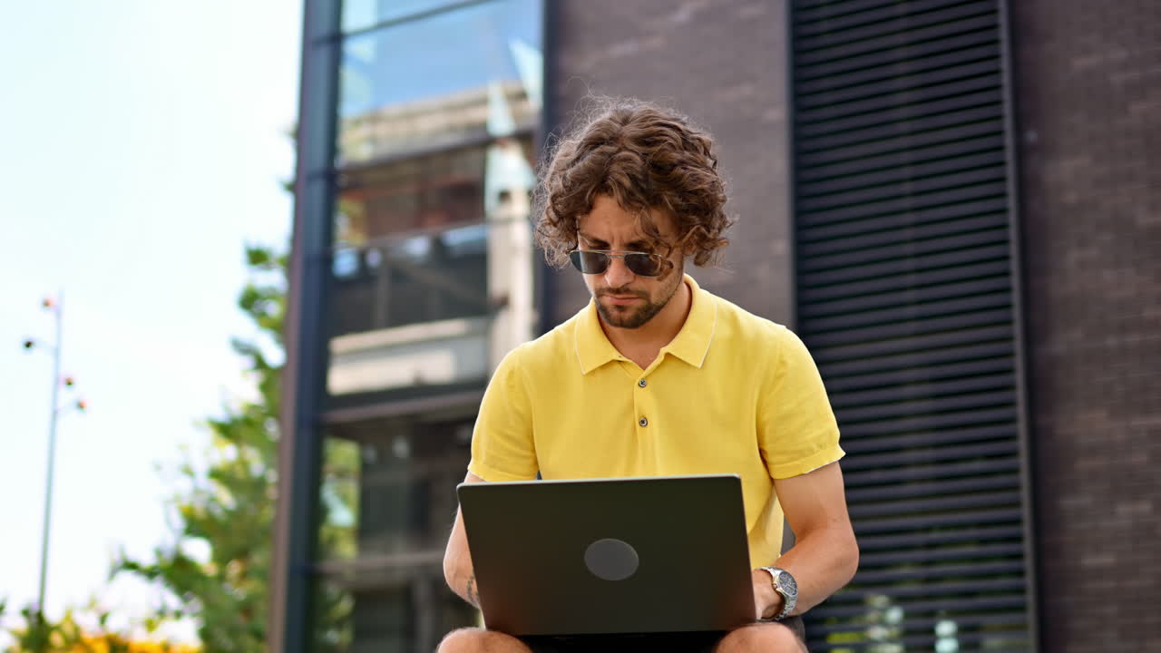 Man in yellow shirt talking standing on a bench and working on a laptop