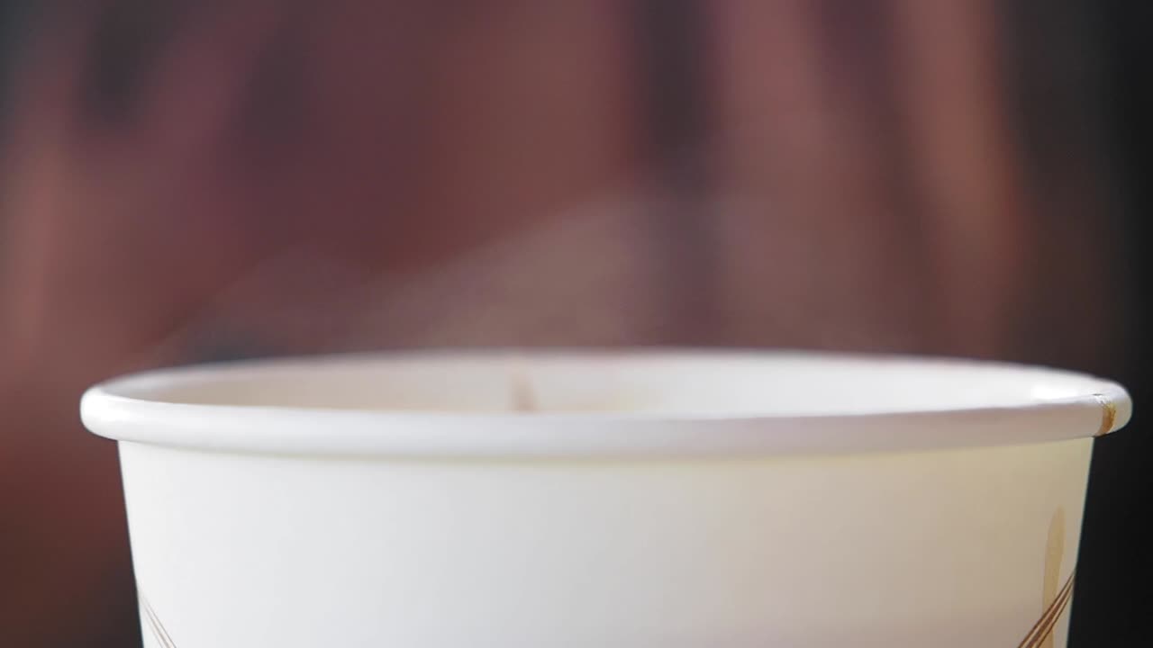 primer plano de una taza de papel blanco con vapor que se levanta de ella