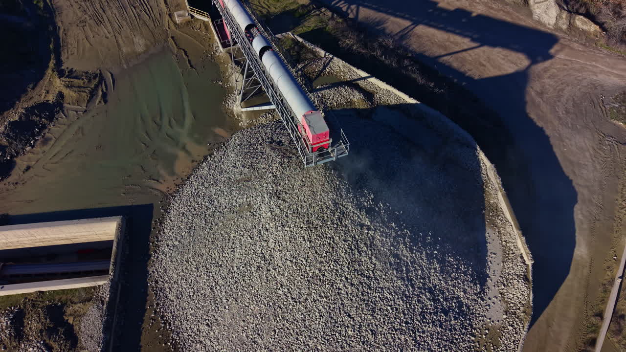 Macchinari pesanti scaricano ghiaia in un cantiere in pieno giorno, mettendo in mostra il trambusto del settore e il movimento dei materiali in un paesaggio trafficato