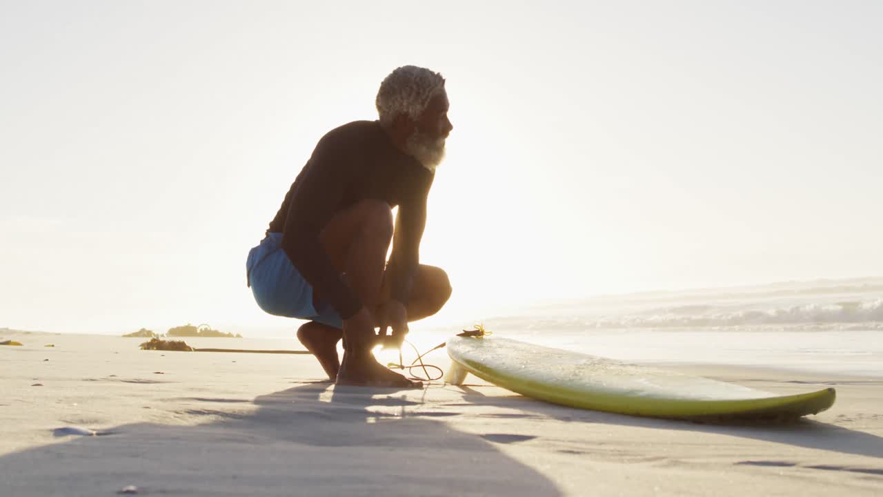 hombre afroamericano de alto nivel preparándose antes de surfear en una playa soleada