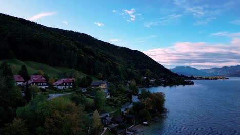 Calm,-blue-lake-surrounded-by-lush-green-mountains-with-houses-nestled-amongst-the-trees-on-the-shore