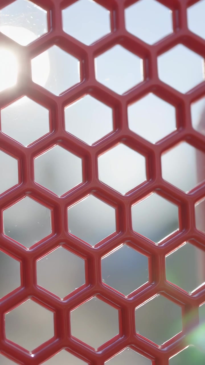 Vídeo vertical: Sol se movendo para o canto superior esquerdo atrás de uma malha hexagonal vermelha no vidro, formando um reflexo de lente