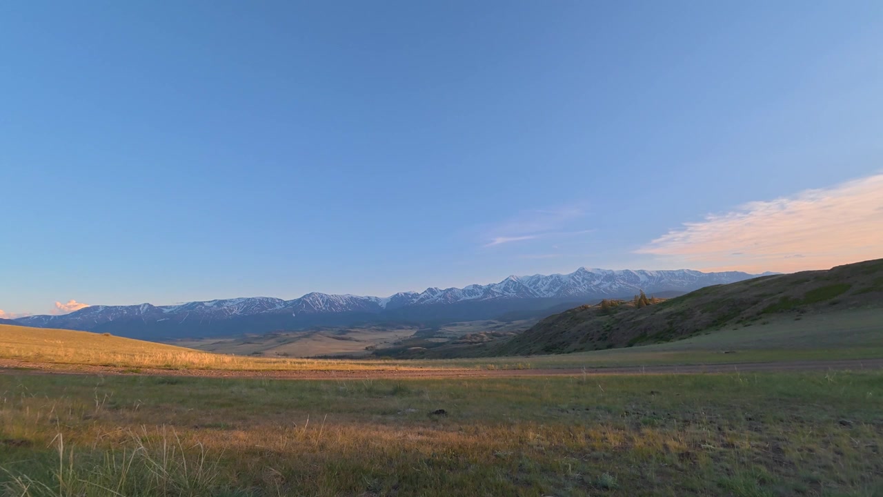 Un time-lapse cattura le montagne dell'Altai e un vasto campo verde al tramonto mentre i colori cambiano nel cielo