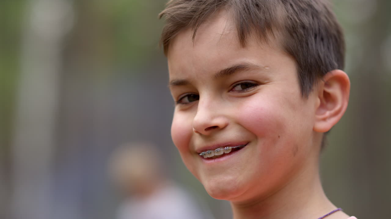 Portrait of teen boy in braces smiling to camera outdoors in forest.