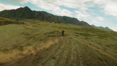 person rides motorcycle along mountain valley fpv. sportsman on motorbike crosses offroad area with training camp. freedom and power of wilderness