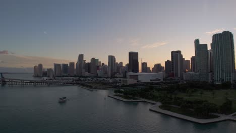 downtown miami cityscape with kaseya centre and park in foreground, aerial pull back establishing shot over water at dusk