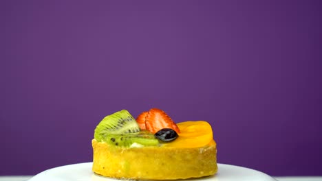 pastry with blueberry, kiwi, orange, strawberries on the plate rotation. violet background.