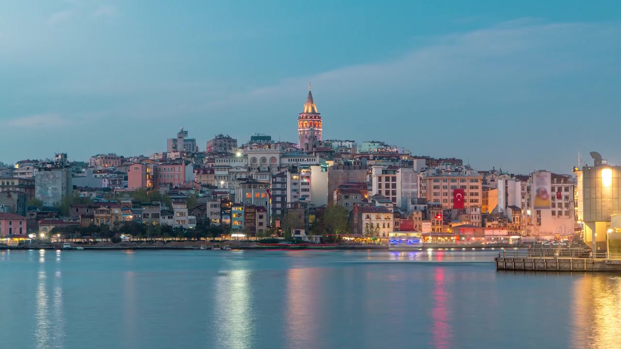 İstanbul'da Galata Kulesi ve çevresinin Haliç Körfezi üzerindeki akşam manzarası, gündüzden geceye geçiş hızlandırılmış çekimi. Bahar gününde bir gemiyle birlikte suya yansıyan aydınlatılmış şehir silüeti.