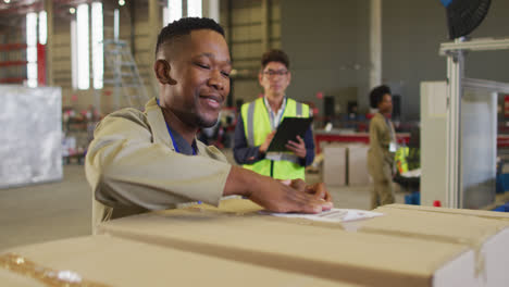 diverse male workers with clipboard and boxes smiling in warehouse