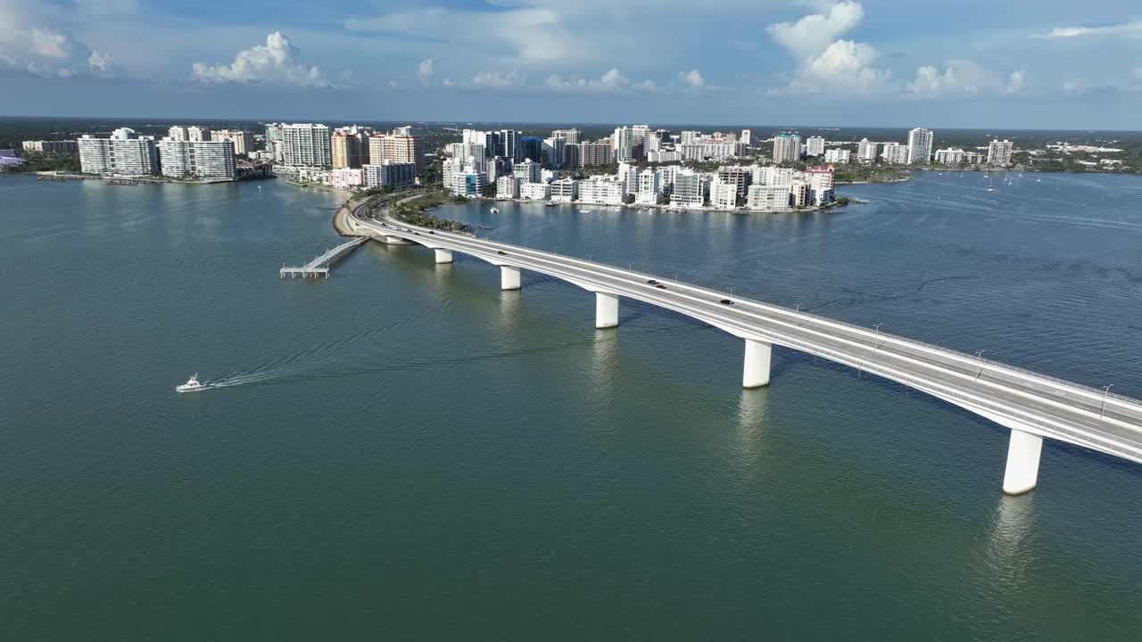 Traffic scene on Ringling Bridge over Sarasota Bay. Sunny day with skyline and high-rise buildings of downtown at sunset. Aerial flyover wide shot. Establishing shot.