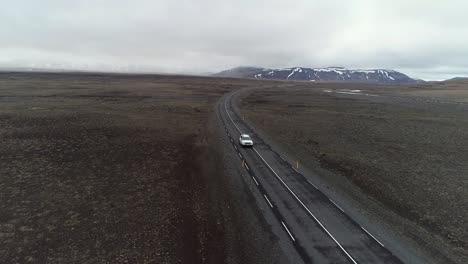 Toma-Aérea-Frente-Al-Auto-Siguiendo-En-El-Valle-Con-Montañas-Al-Fondo