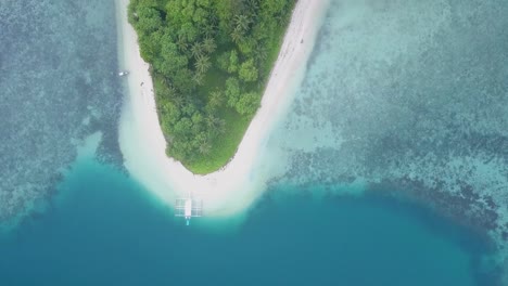 aerial view of perfect blue waters tracking to secluded tropical island and white beach with traditional filipino boat in the philippines