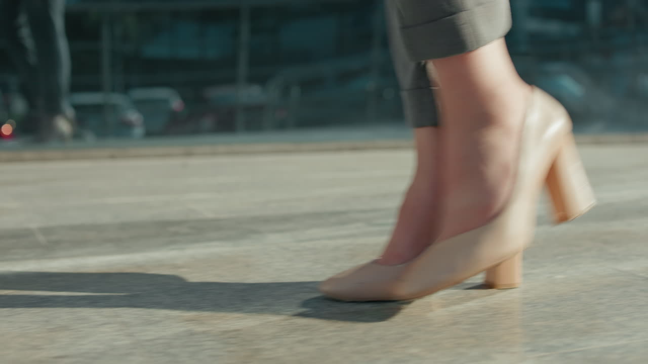 Close up side leg view of elegant lady walking gracefully in nude high heels along modern urban walkway with sunlight reflecting off glass building