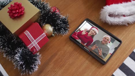 Smiling-caucasian-father-with-daughter-wearing-santa-hats-on-christmas-video-call-on-tablet