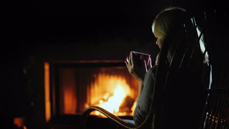 drinking hot tea by the fire the woman resting at home near the fireplace where the fire is burning