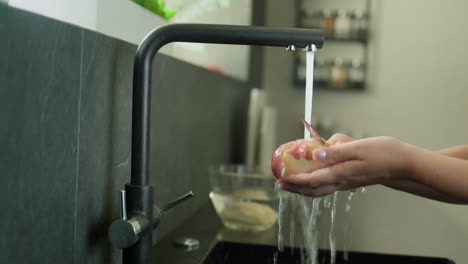 las manos de las mujeres cortan la cáscara de una patata bajo el agua corriente