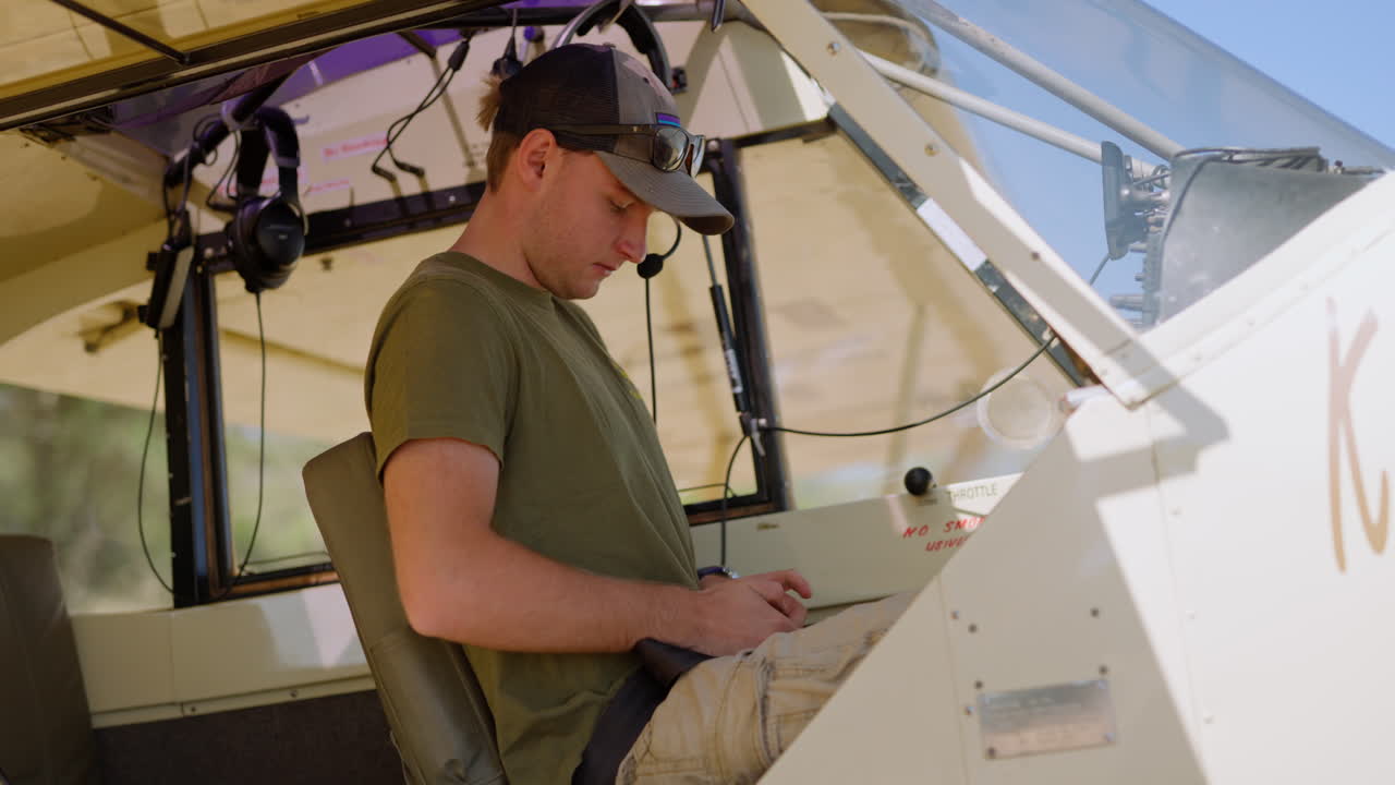 Giovane uomo che allaccia la cintura di sicurezza nella cabina di pilotaggio di un piccolo aereo.