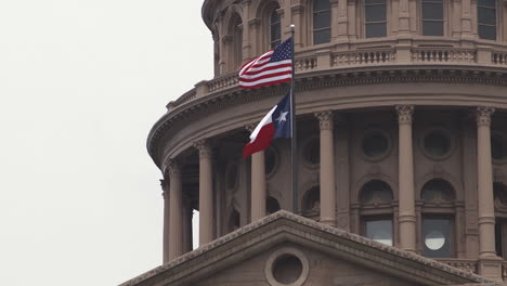 close-up of u.s. and texas flags waving above texas state capitol in austin, texas